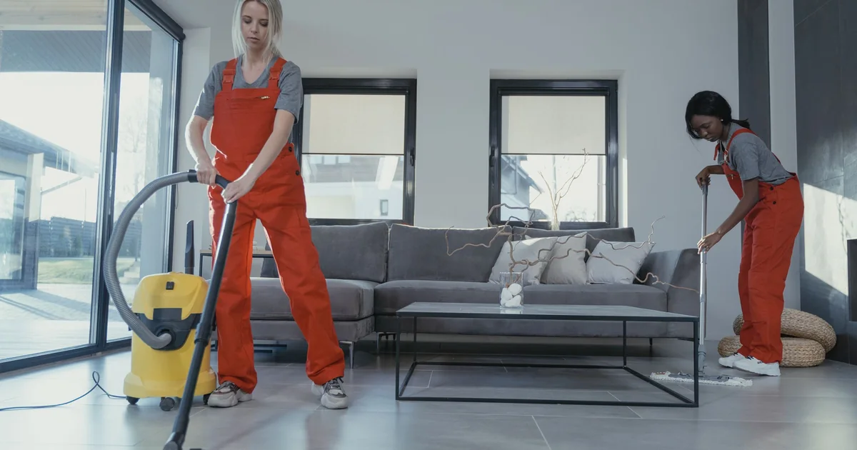 Two uniformed cleaners vacuuming and mopping a living room during a booked cleaning visit